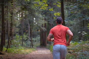 Back view of a Caucasian man in sportswear running along a forest trail, close up
