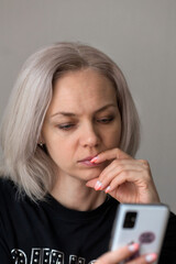 Portrait of a girl with blonde hair. A woman in a black T-shirt.A woman of European appearance with natural makeup.A woman looks at something on her phone.A woman writes a text message in a smartphone