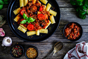 Rigatoni with delicious stew  - aubergine with tomatoes and black olives on wooden table
