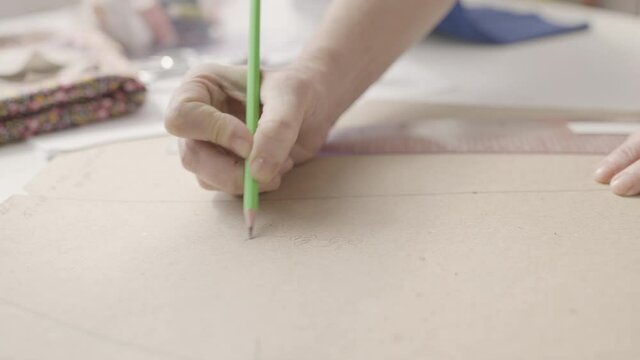 Seamstress writing notes on sewing pattern, making clothes in fashion studio