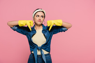 Upset housewife in rubber gloves showing dislike isolated on pink