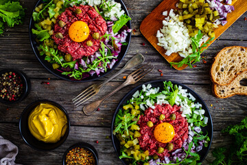 Perfect beef tartare steak with onion, capers, pickled cucumbers and mushrooms on wooden table
