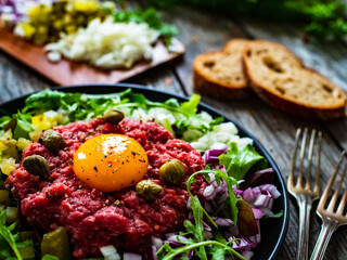 Perfect beef tartare steak with onion, capers, pickled cucumbers and mushrooms on wooden table
