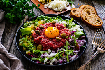 Perfect beef tartare steak with onion, capers, pickled cucumbers and mushrooms on wooden table
