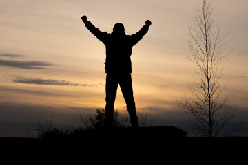 Fototapeta na wymiar silhouette of a winner man throwing his hands up standing on a mountain