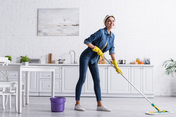 Young woman smiling while washing floor with mop in kitchen