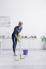Happy housewife cleaning floor with mop in kitchen