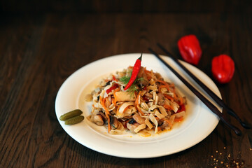 Noodles salad with shrimps on a white plate and sticks. Spicy Korean-style salad on a wooden table.