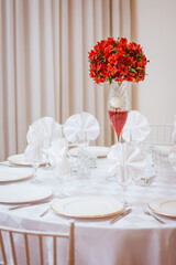 White party table decorated with glasses and red flowers