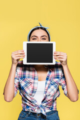 Housewife holding digital tablet near face isolated on yellow