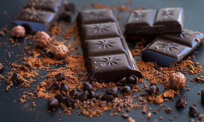 Broken chocolate bar pieces and cocoa powder on dark table