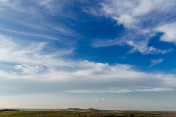 White clouds stretched across the blue sky on a warm sunny day, and under the sky were green fields and hills