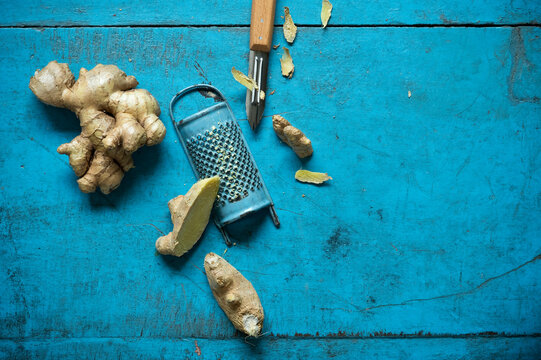 Ginger root, grater and kitchen knife lying on blue wooden surface