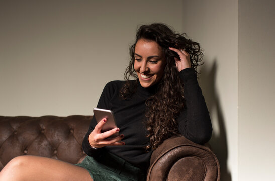 Smiling female freelancer text messaging through phone while sitting on sofa in coffee shop
