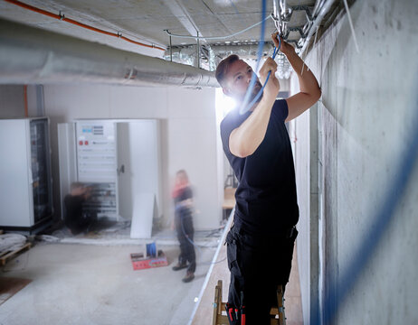 Male electrician installing cables on ceiling in while working in workshop