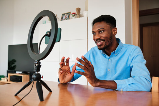 Male influencer vlogging through mobile phone with ring light at home