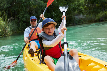 Cute boy and father canoeing in lake during vacation