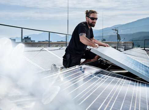 Male electrician installing solar panels on building terrace during sunny day