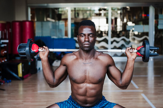 Shirtless Young Male Athlete Exercising With Barbell During Strength Training In Health Club