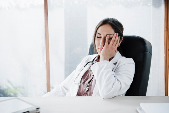 Tired female doctor with eyes closed sitting at desk