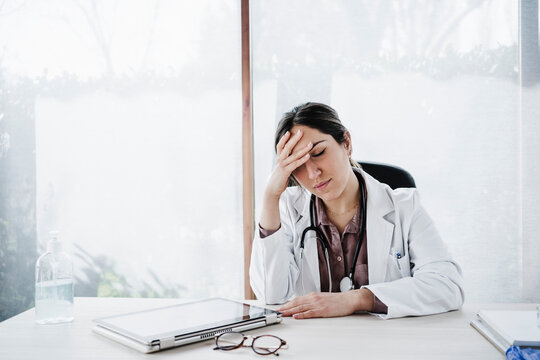 Worried female medical professional with head in hand sitting at desk in hospital