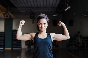 Beautiful female athlete flexing muscles in gym