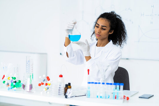 Young female chemist examining liquid in flask in laboratory