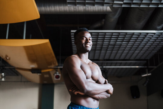 Shirtless sportsman smiling with arms crossed in gym