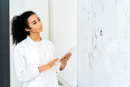 Female researcher with digital tablet examining diagram on whiteboard in laboratory
