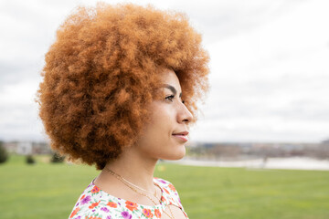 Redhead woman with afro hairstyle looking away at park
