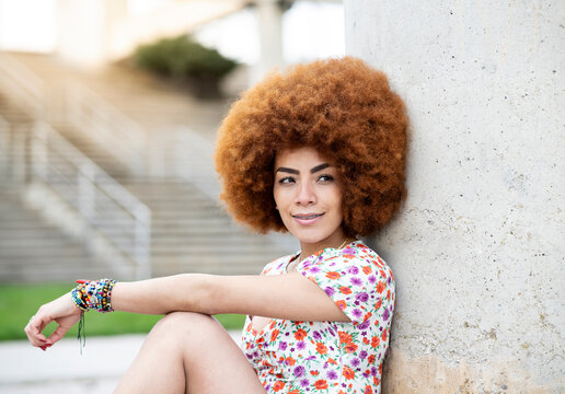 Smiling woman with hand on knee leaning on wall