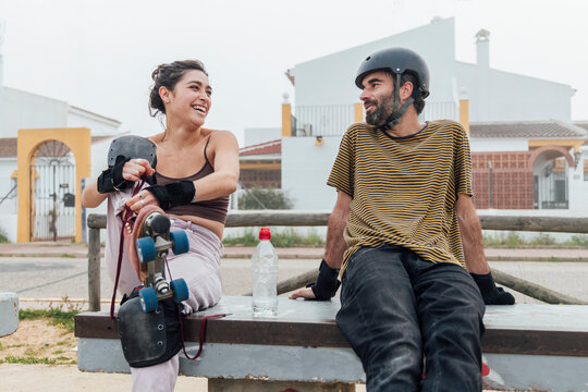 Cheerful woman with roller skates looking at man while sitting on bench