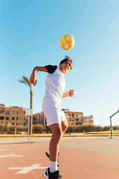 Boy heading soccer ball on sports court against sky