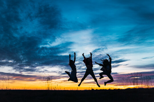 Carefree female friends with arms raised jumping in front of sky