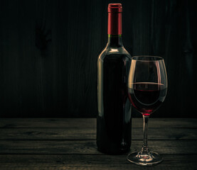 Bottle of red wine with a glass of red wine on an old wooden table