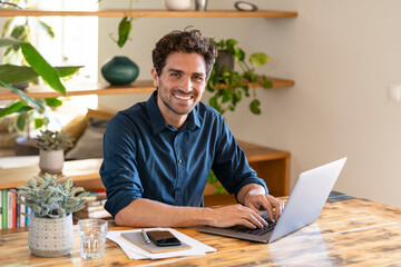 Happy male freelancer working from home through laptop