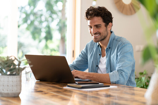 Smiling freelance worker using laptop while sitting at table