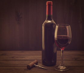 Bottle of red wine with a glass and corkscrew on an old wooden table