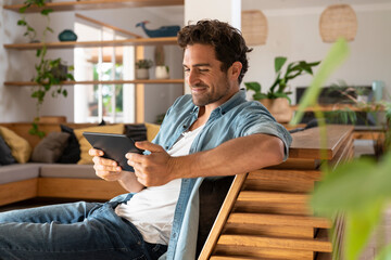 Smiling mid adult man looking at digital tablet while sitting on couch at home