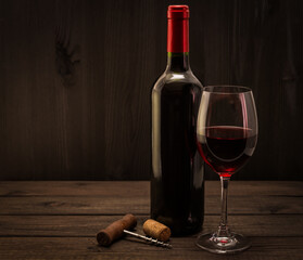 Bottle of red wine with a glass and corkscrew with cork on an old wooden table