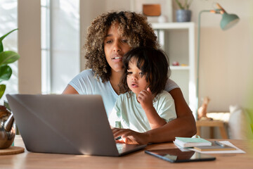 Mother and toddler daughter looking at laptop together while working from home