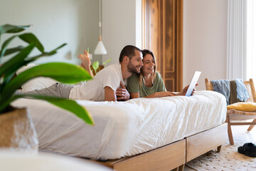 Young couple using laptop while lying on bed in bedroom at home