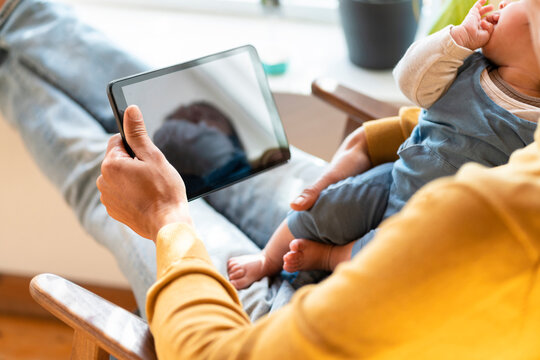 Father holding tablet and sleeping baby at home