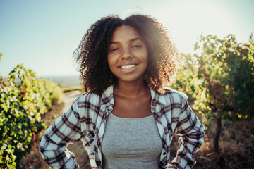 Beautiful mixed race female farmer smiling while standing in vineyard of farm - Powered by Adobe