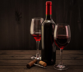 Two bottles of red wine with a glass and corkscrew with cork on an old wooden table