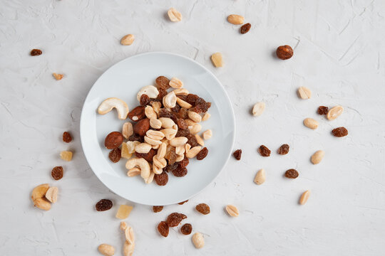 Mixed Nuts Hazelnut Peanut Raisin On A White Plate And Scattered Side By Side On A Light Gray Concrete Textured Background