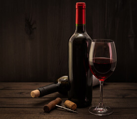 Two bottles of red wine with a glass and corkscrew with cork on an old wooden table