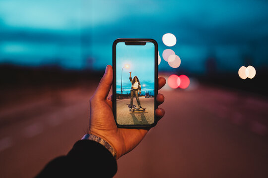 Young man photographing woman on skateboard during dusk