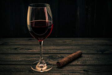 Glass of red wine and cuban cigar on an old wooden table. Focus on the cuban cigar