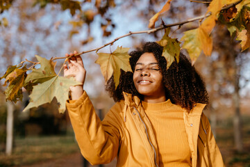Afro woman holding branch in park during autumn